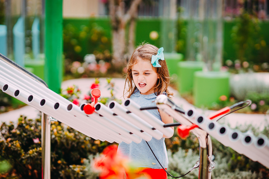 a young girl smiling a playing a large silver musical instrument in a park or playground