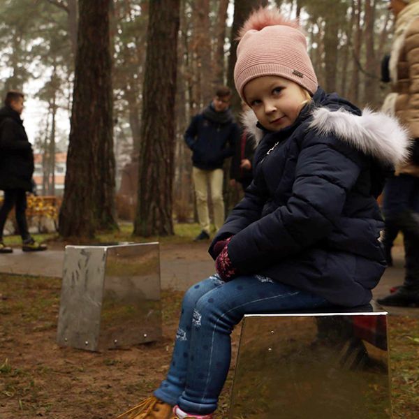 Little girl in bobble hat sat on a stainless steel cajon drum in a city park