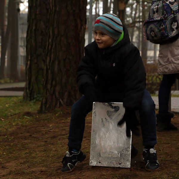 Little boy wearing a winter hat playing a large silver musical instrument in a park