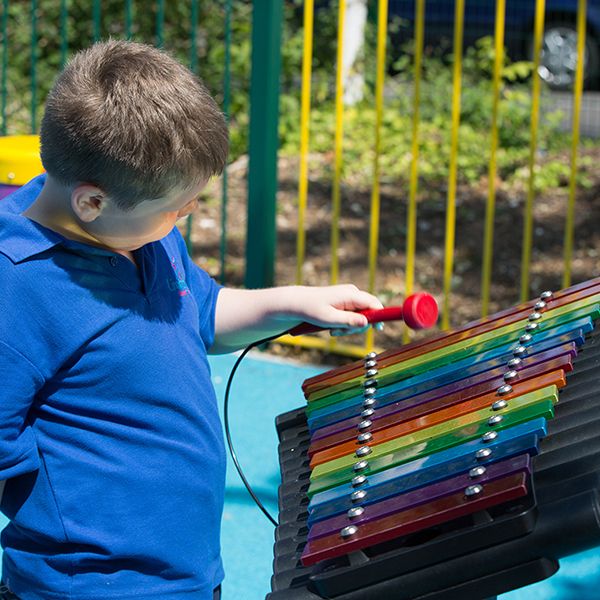 boy with special needs playing colourful outdoor drums in a school playground