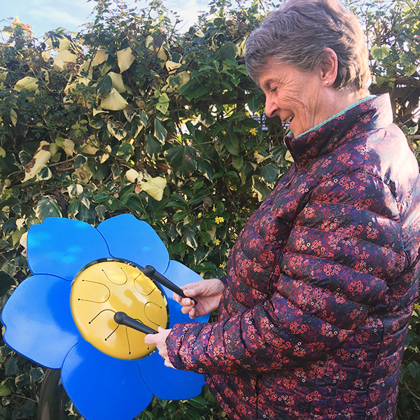 older lady playing a colorful outdoor drum shaped like a forget me not flower in a senior living center