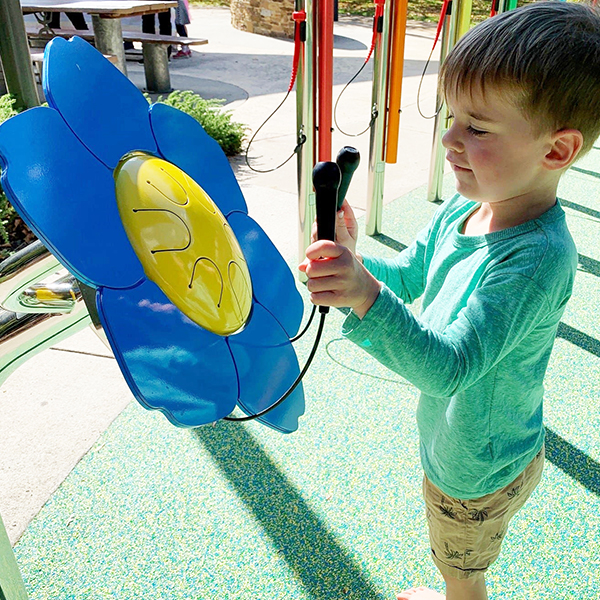 A young barefoot boy in a playground playing an outdoor drum shaped like a forget me not flower