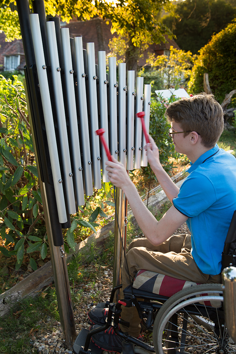 young man in a wheelchair playing a vertical outdoor musical instrument