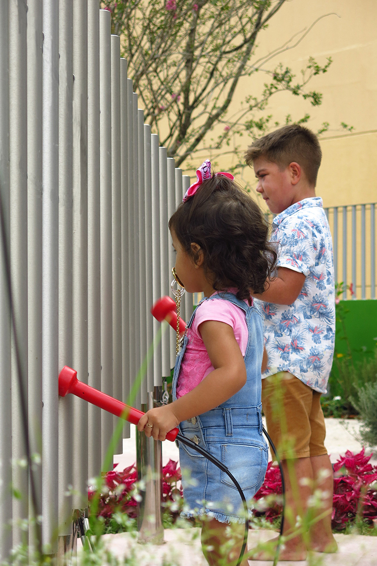 a young girl and taller boy playing a set of large outdoor musical chimes in a music park or playground