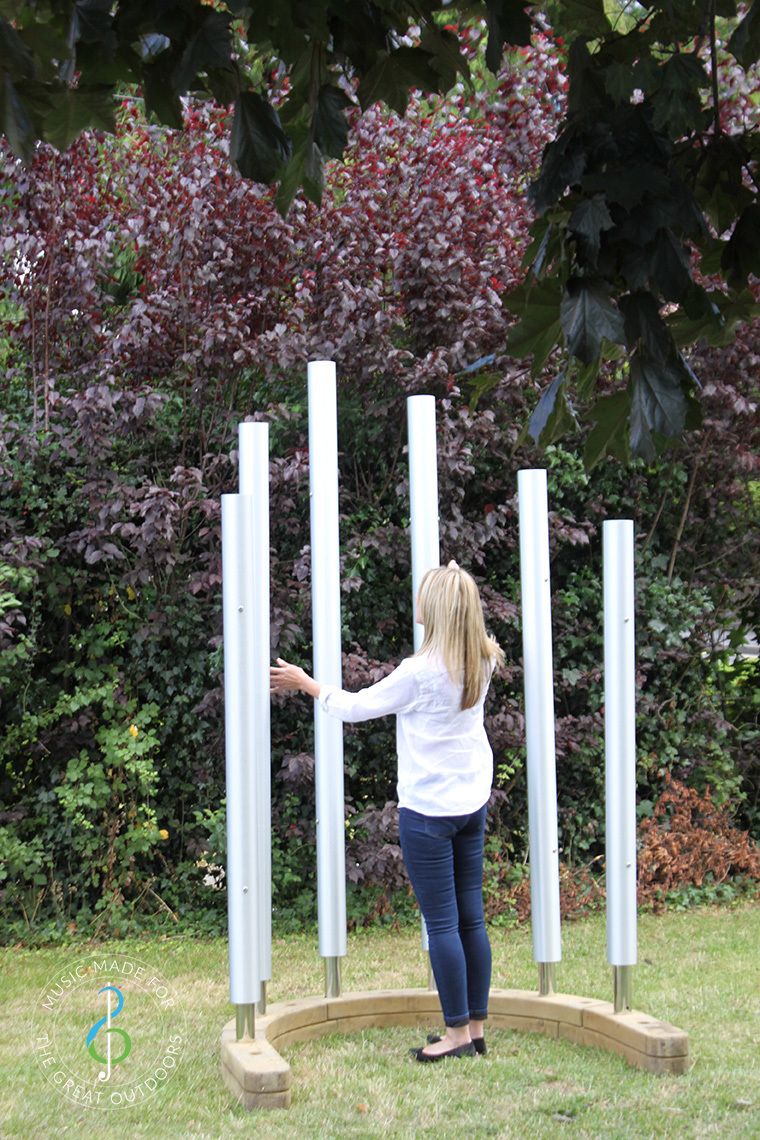 Lady playing six large chimes on a horsehoe shaped timber base with her hands