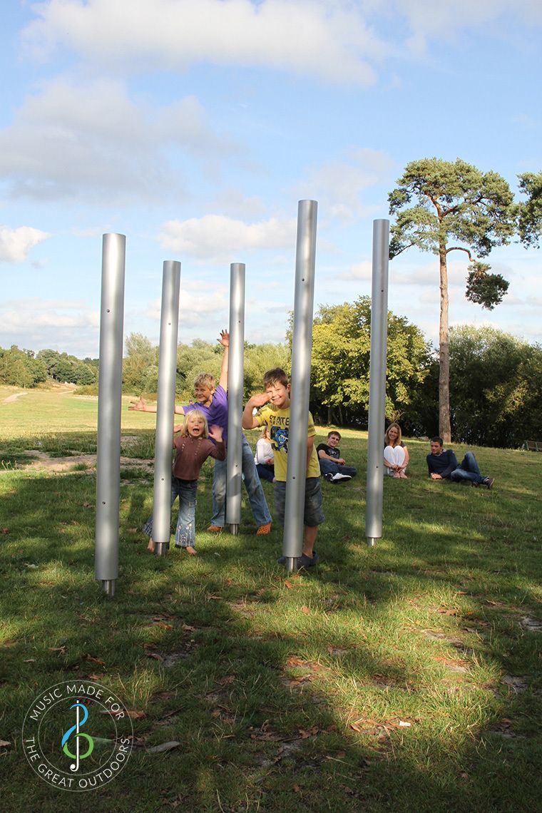 Family playing on five large outdoor chimes together in the park