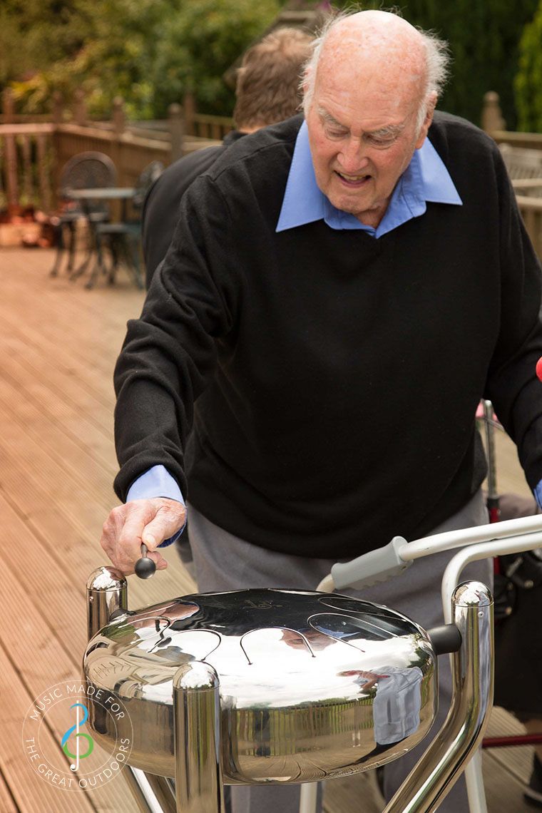 Older Man Playing Stainless Steel Tongue Drum in Garden