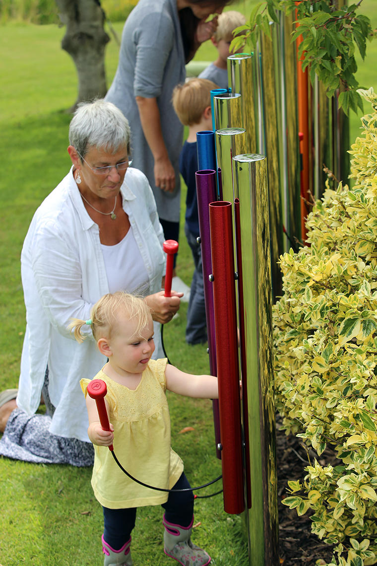 A family playing on a set of rainbow colored calypso chimes in a musical garden