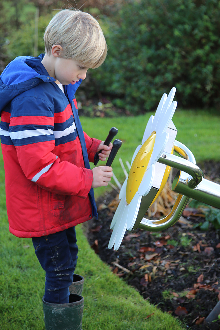 A young boy playing an outdoor musical drum in the shape and colours of a daisy