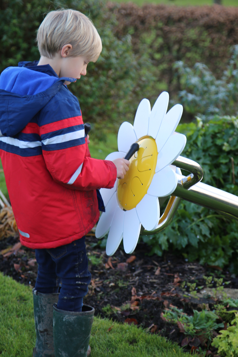 A young boy playing an outdoor musical drum in the shape and colours of a daisy