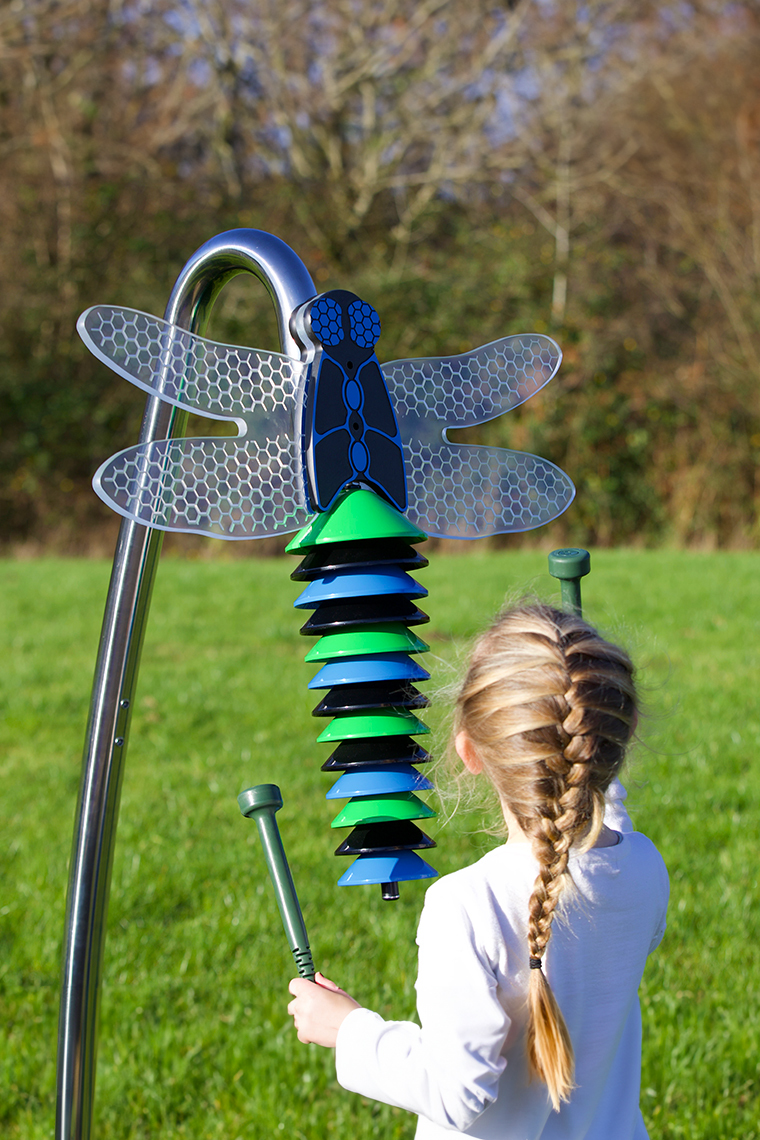 an outdoor musical instrument shaped like a dragonfly being played by a young girl