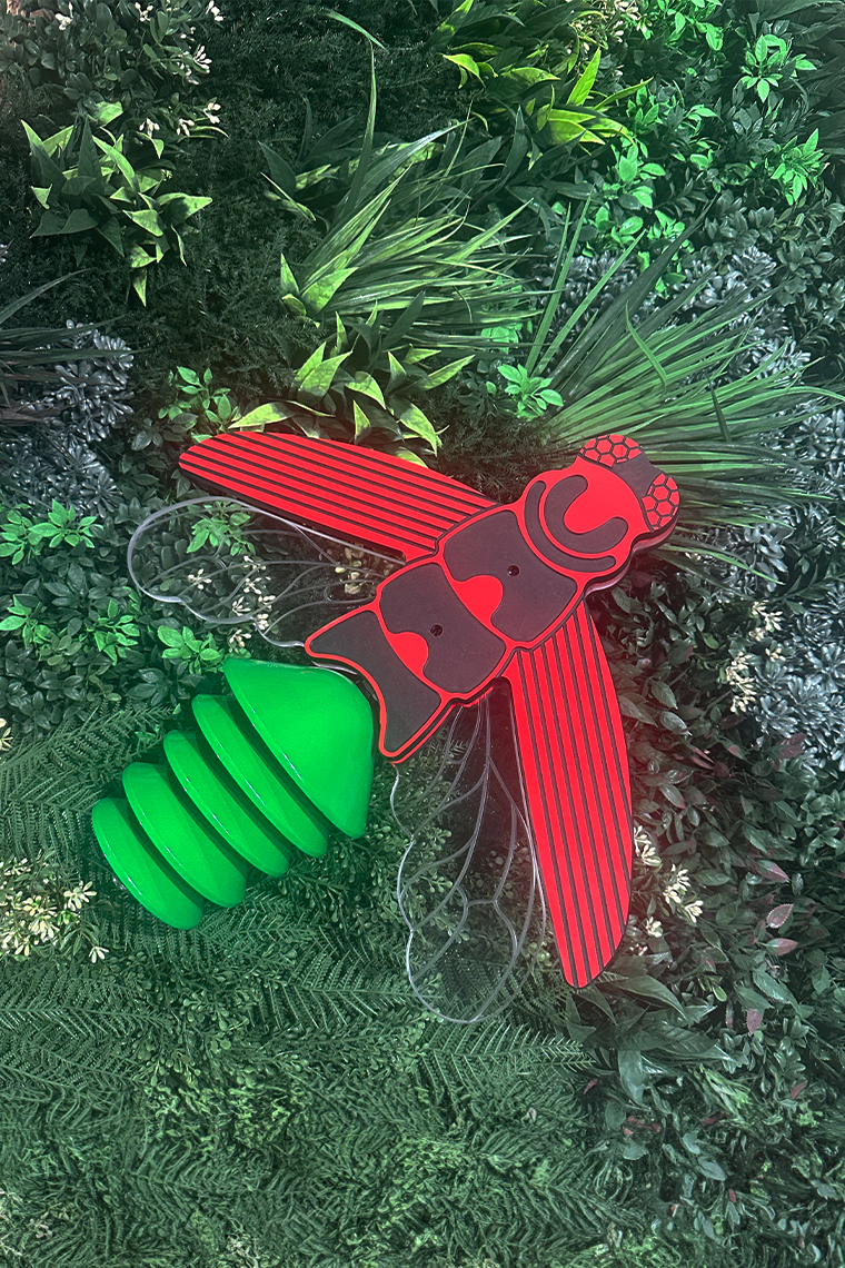 an outdoor musical instrument shaped like a firefly with green bells as a tail, clear acrylic wings and HPL red and black body