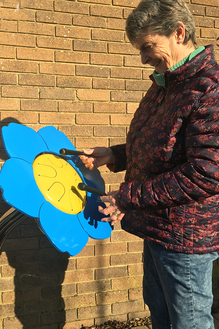 older lady playing a colorful outdoor drum shaped like a forget me not flower in a senior living center