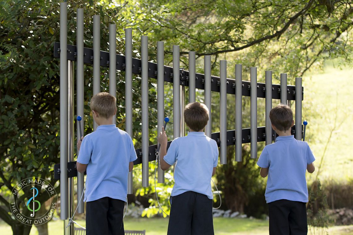 three schoolboys in blue uniform playing on outdoor musical chimes in playground