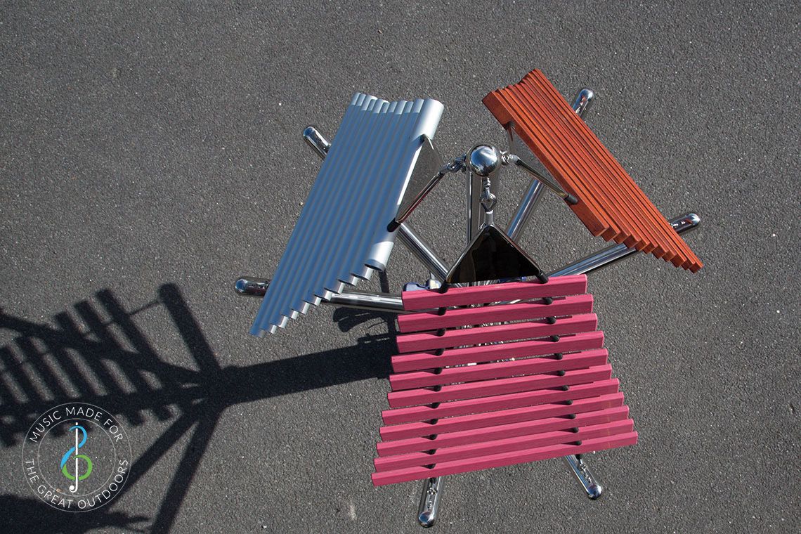 looking down onto large outdoor musical instrument with one stainless steel post in ground with three vertical xylophones attached