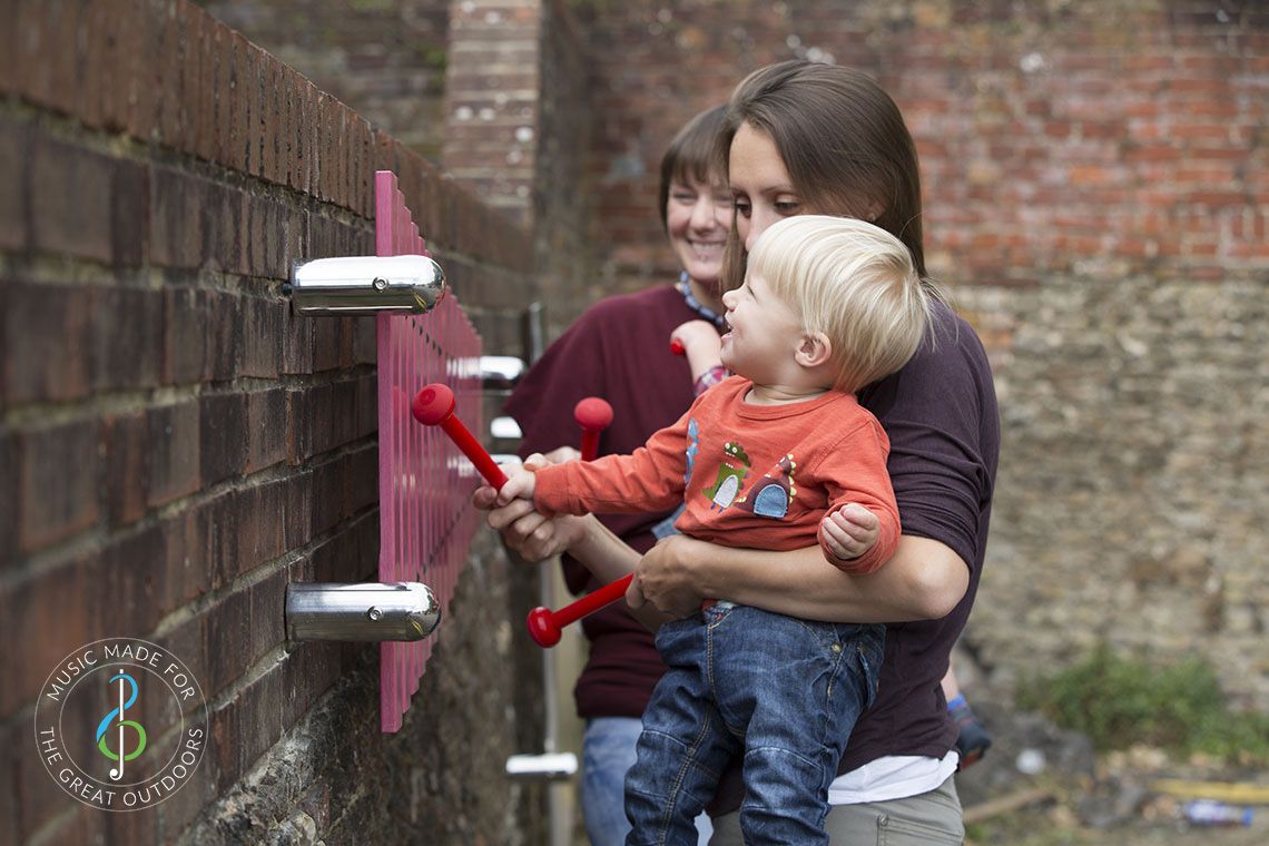 laughing baby being held up by mother to play on wall mounted marimba xylophone 