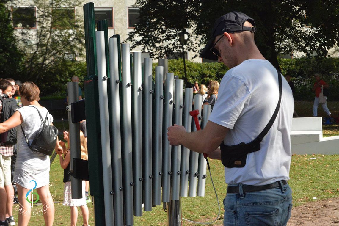 Young man playing large vertical xylophone in a park