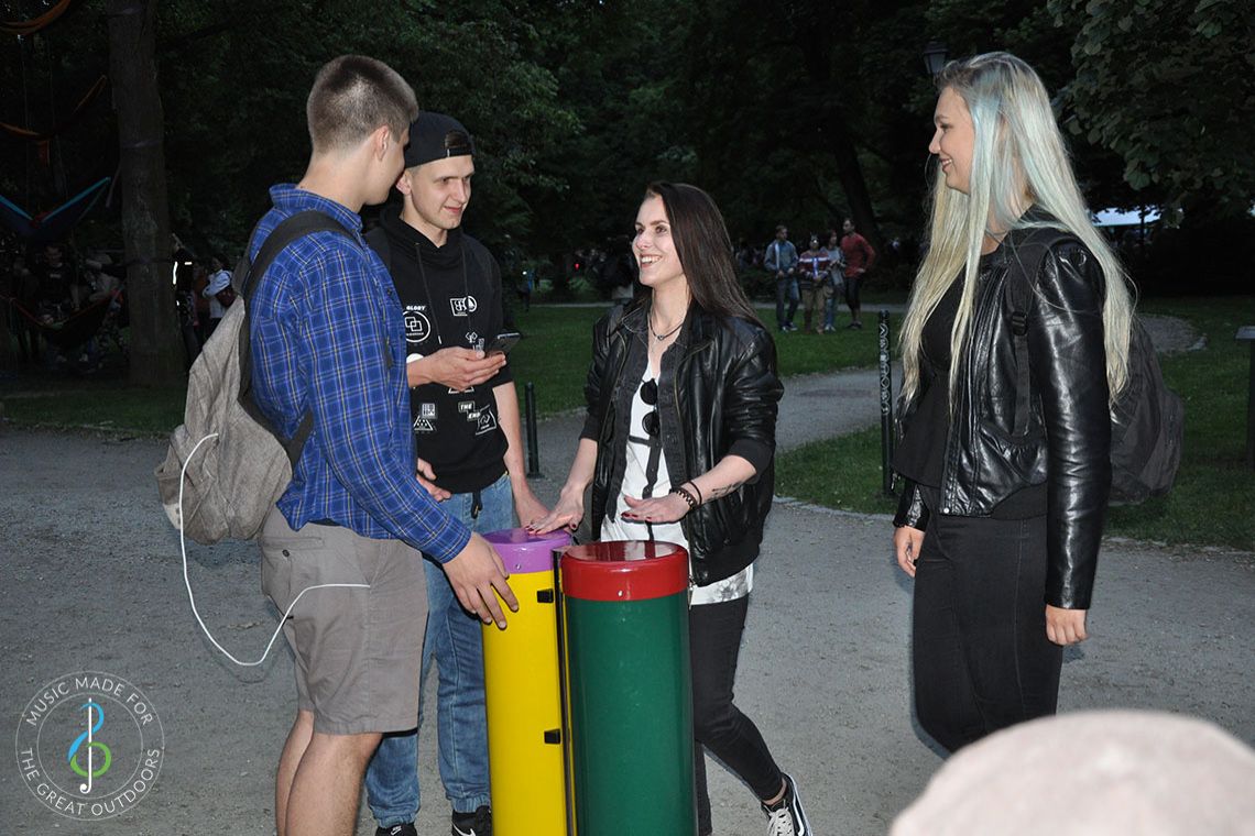 Four older teenagers laughing and playing pair of conga drums in music playground at dusk