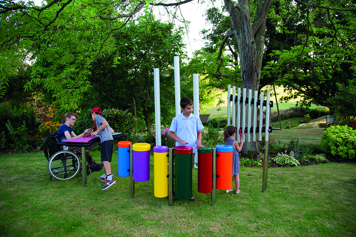 group of four children playing on an ensemble of outdoor musical instruments in a park