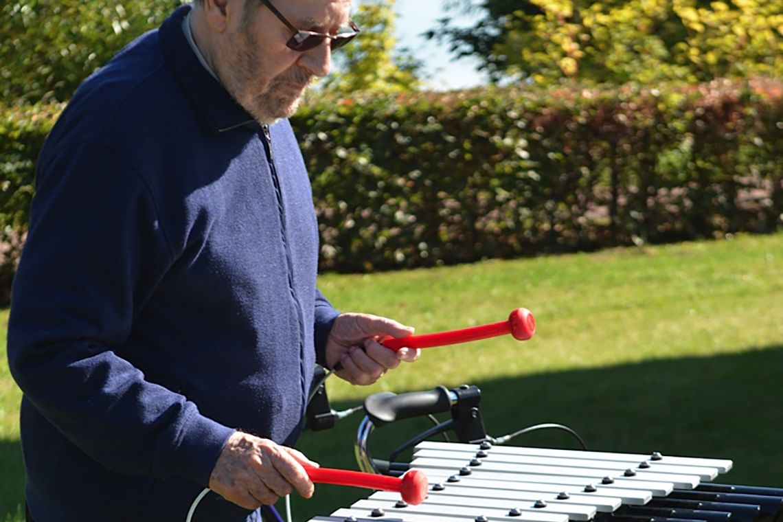 Older man playing an outdoor xylophone in care gome garden