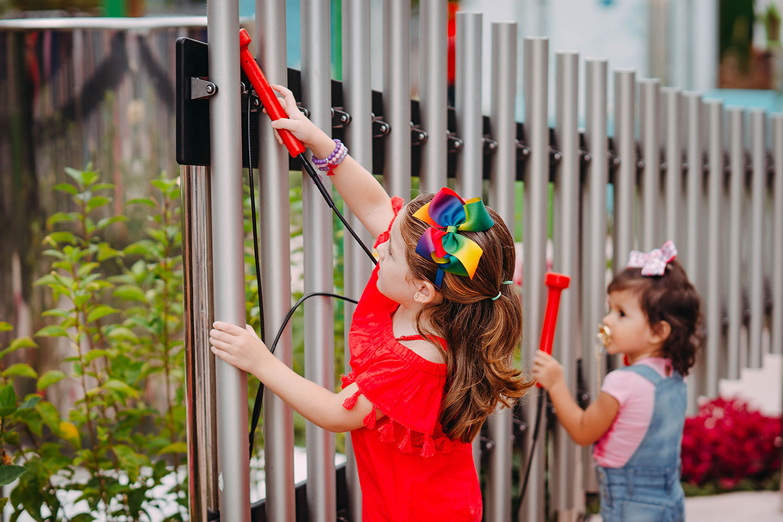 two little girls playing a set of large aluminium musical pipes or chimes in a music park or playground