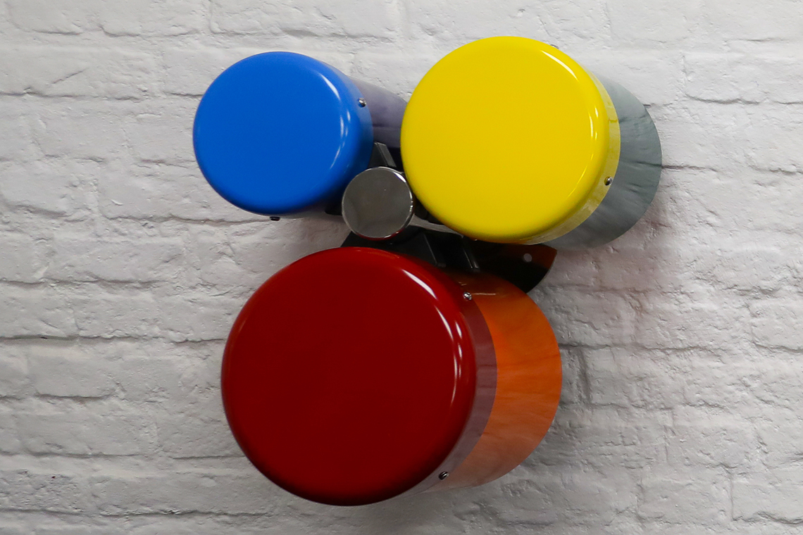 A group of three different sized wall mounted rainbow coloured outdoor bongo drums designed for smaller children