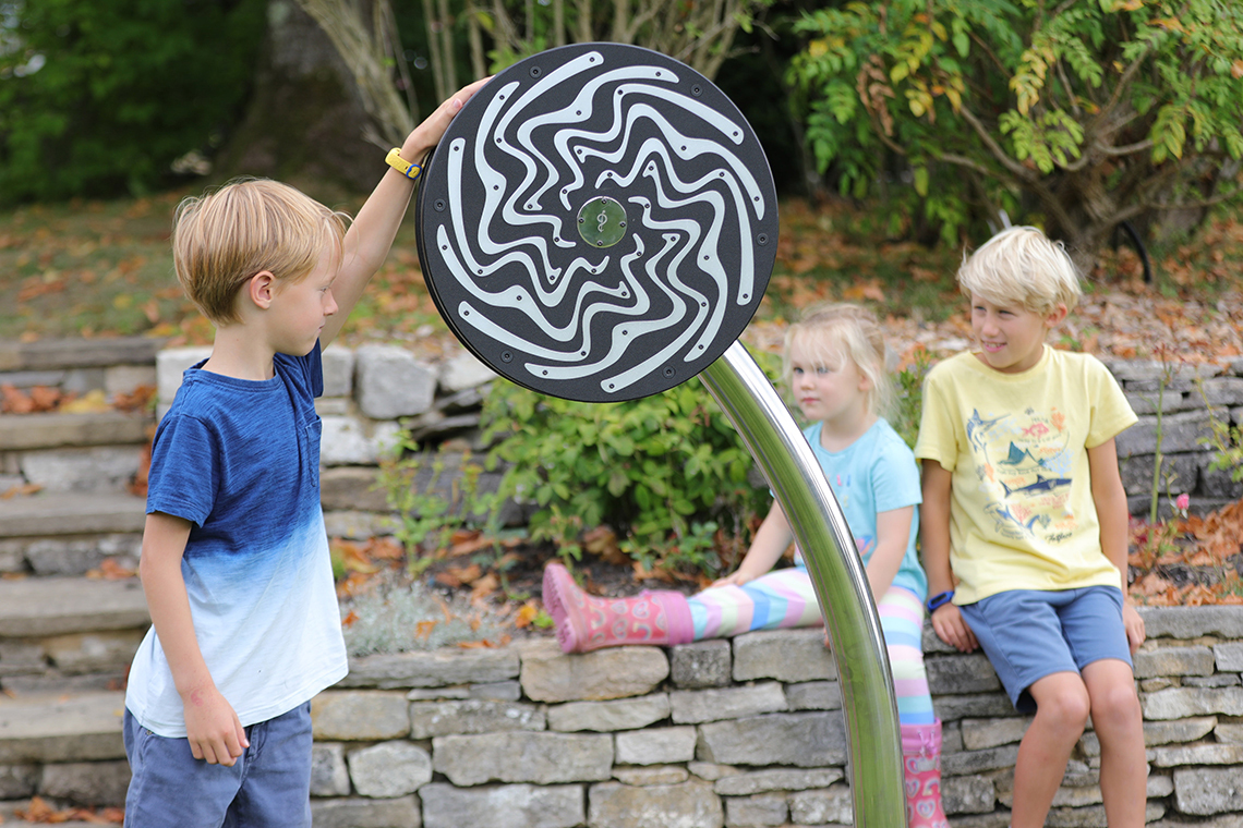 a young boy spinning a large rain wheel in a park 